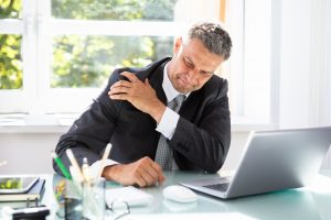 Douleur d'un salarié à l'épaule en train de travailler, assis à son bureau. 